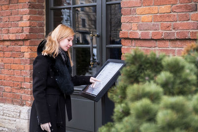 Young woman using laptop while standing against brick wall