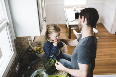 High angle view of father cooking food while daughter having fruit in kitchen