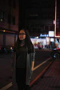 Young woman with hands in pockets walking on street at night