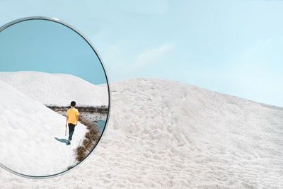 Reflection of man walking at beach against sky