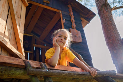 Girl plays in creative handmade treehouse in backyard, summer activity, happy childhood, cottagecore