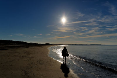 Rear view of silhouette man on beach against sky during sunset