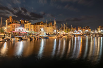 Sailboats in harbor by buildings in city at night