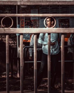 Portrait of young man standing by metal grate