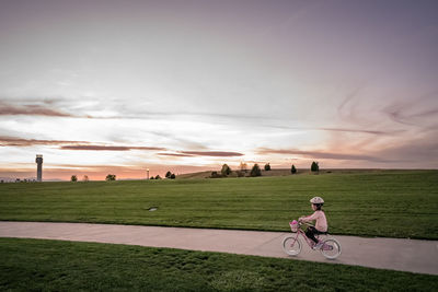 Young girl bikes near a grassy hill at sunset