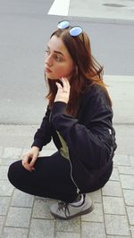 Teenage girl looking away while crouching on footpath
