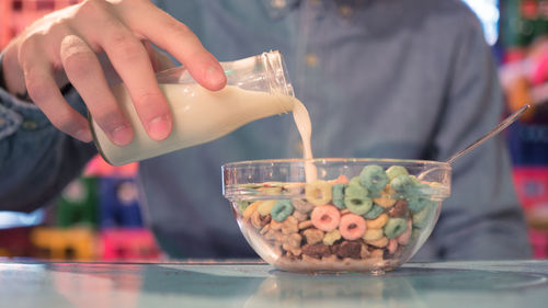 Close-up of man pouring milk from bottle in breakfast bowl