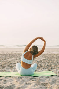 A young woman practices yoga in the lotus position on the shore of the poria, rear view