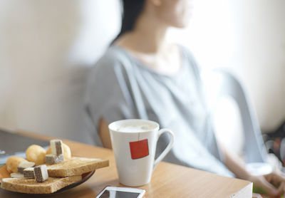 Close-up of coffee and food on table while woman sitting on chair against wall