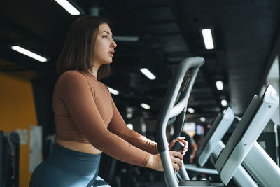 Young brunette woman training for cardio equipment at fitness gym