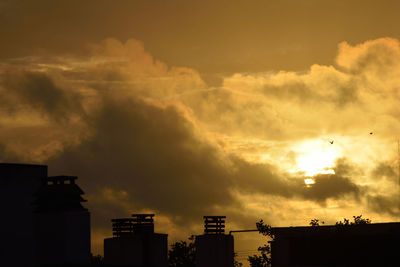 Silhouette houses against dramatic sky during sunset