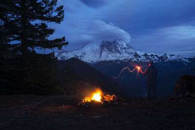 Rear view of man holding burning stick against snowcapped mountains