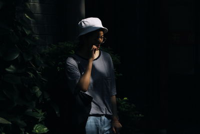 Man wearing hat standing against plants at night