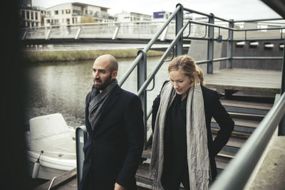 Mid adult businessman and businesswoman walking down stairs by river