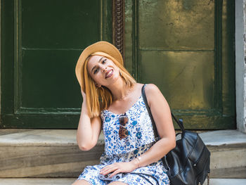 Portrait of smiling young woman sitting against wall