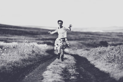 Woman running on dirt road against clear sky