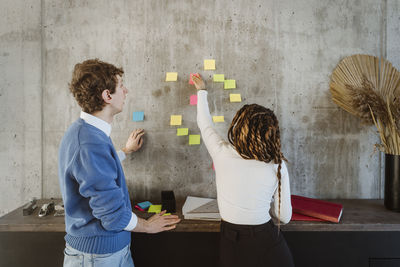 Male and female colleagues discussing over adhesive notes on wall in creative office