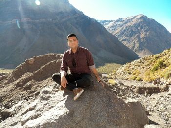 Portrait of young man sitting on mountain during sunny day