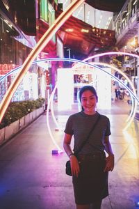 Portrait of smiling woman standing against illuminated decoration at night