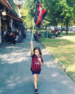 Full length portrait of girl holding flag while walking on street