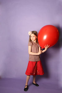 Girl standing with balloon against purple background