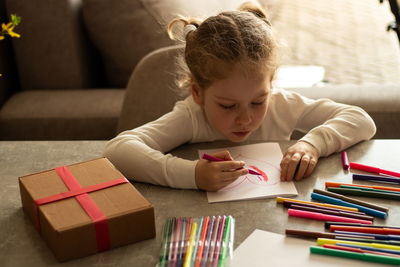 Cute 4-year-old blonde girl concentrates while drawing sitting at table. childhood creativity