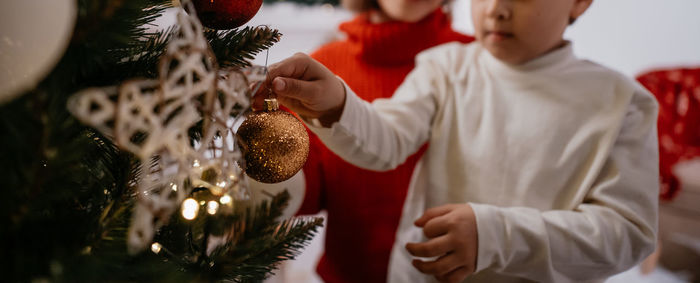 Cropped view of happy boy decorating christmas tree with his mother during cozy home evening