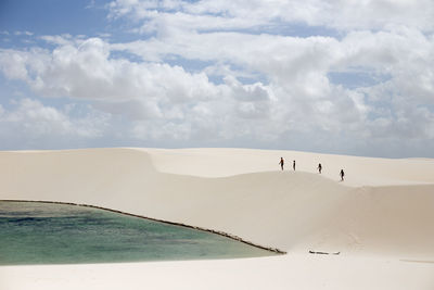 People walking on sand against cloudy sky