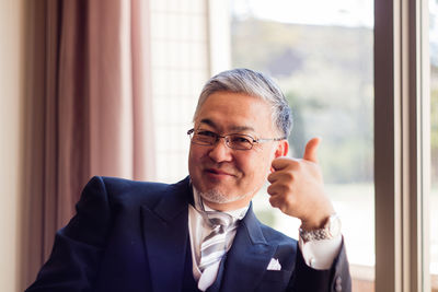 Portrait of smiling man showing thumbs up while sitting at home