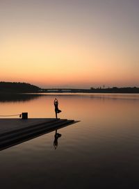 Silhouette woman doing yoga at beach against sky during sunset