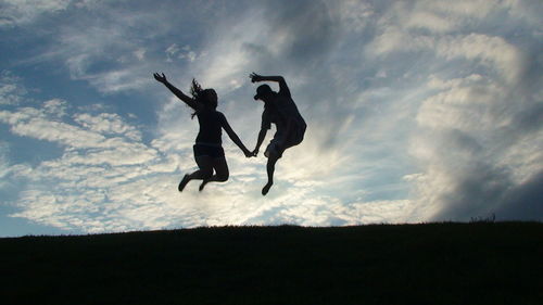Silhouette people jumping against sky