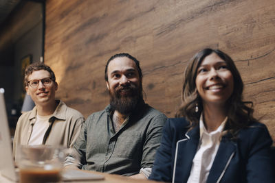 Smiling business colleagues looking away while sitting together in board room