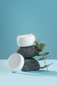 White jar of cream on gray stones with a sprig of eucalyptus on a blue background. cosmetics.