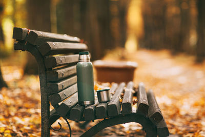 A tourist thermos with a cup stands on a bench in an autumn park