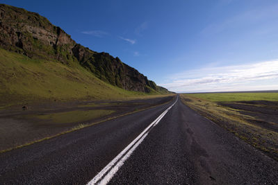 Empty road by field against sky