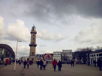 People walking in city against cloudy sky