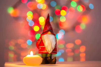 Close-up of figurine by illuminated candle on table during christmas
