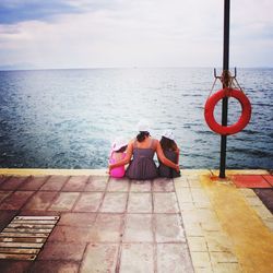 Rear view of family sitting at beach against sky