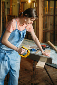 Woman working with wood in workshop. measuring plunk, drilling holes, sewing wood. reuse, reduce