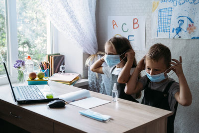 Back to school safety. schoolkids wearing masks and using antiseptic in classroom at school