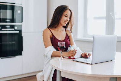 Young woman using phone while sitting on table at home