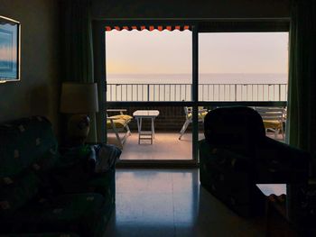 Chairs and table by sea against sky during sunset