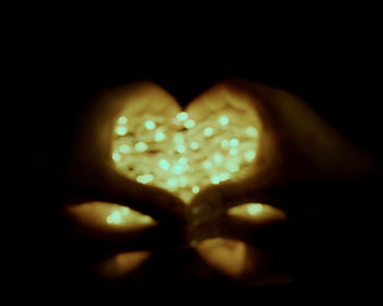 Close-up of hand holding heart shape against black background