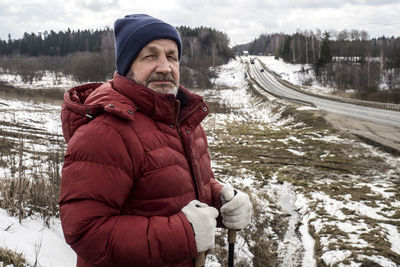 An elderly man stands by the highway in winter