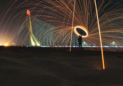 Light trails on illuminated bridge against sky at night