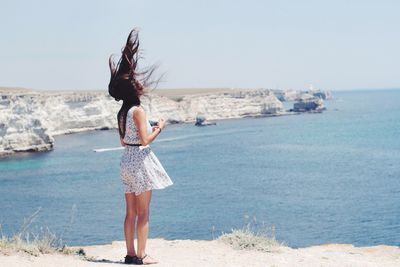 Rear view of woman standing on beach against clear sky