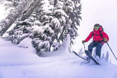 Man jumping from top of snowy hill while backcountry skiing in bc