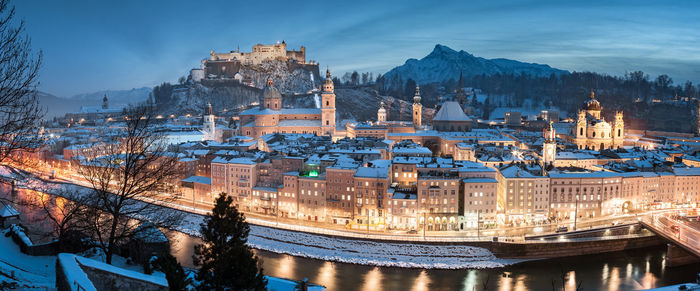 Panoramic view of illuminated townscape by river during sunset