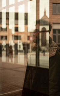 Reflection of man standing on street against building in city