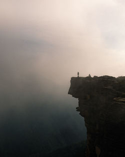 Mid distance view of person standing on mountain against sky during foggy weather